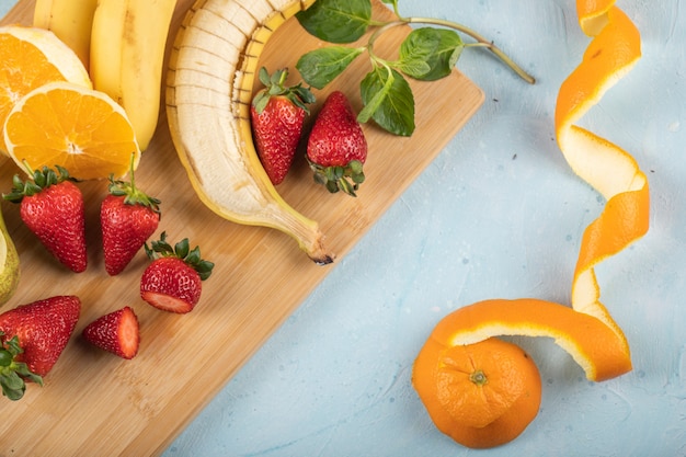 Frische Bananen, Orangen und Erdbeeren an einer blauen Wand, serviert mit Minzblättern