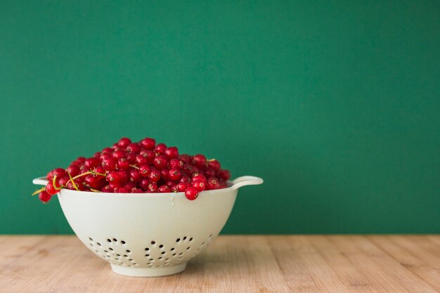 Frische Beeren der roten Johannisbeere im Sieb auf Schreibtisch vor grünem Hintergrund