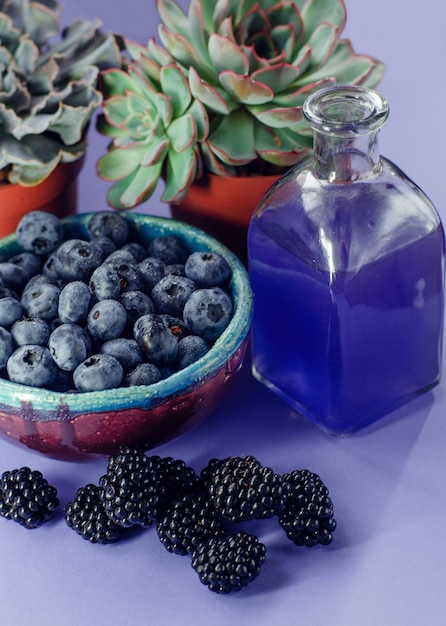 Frische Beeren. Heidelbeeren in einem Teller, Blumen, Brombeeren mit Glas Saft und Himbeeren auf blauem Hintergrund.