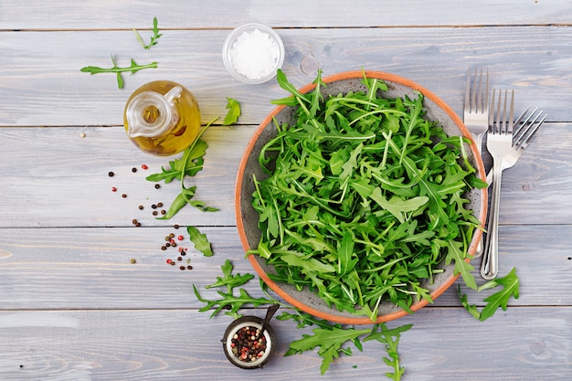 Frische Blätter von Arugula in einer Schüssel auf einem hellen hölzernen Hintergrund. Flach liegen. Ansicht von oben