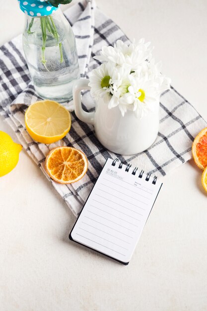 Frische Blumensträuße im Vase und Pitcher in der Nähe von Früchten und Notizblock auf Serviette