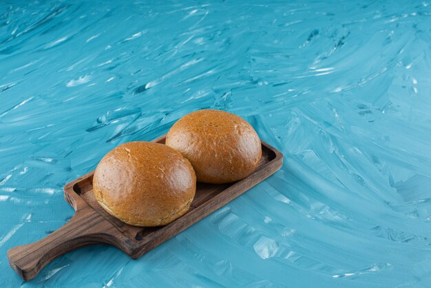 Frische braune Brötchen in einem Holzbrett auf hellem Hintergrund.