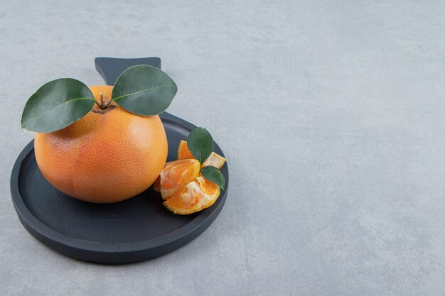 Frische Clementine und Segmente auf schwarzem Teller.