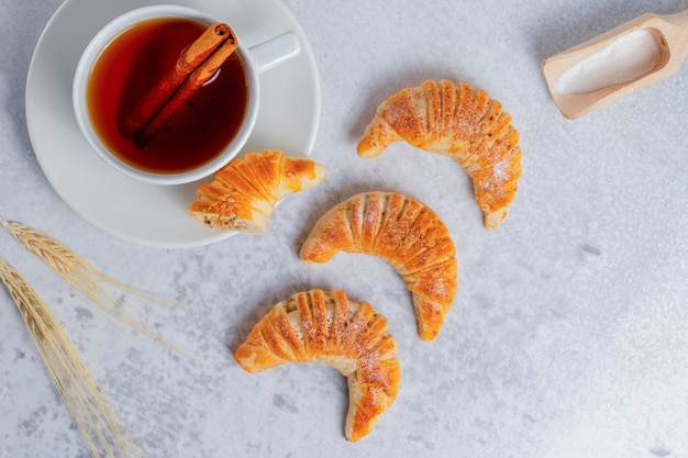 Frische croissants mit duftendem tee auf grauer oberfläche.