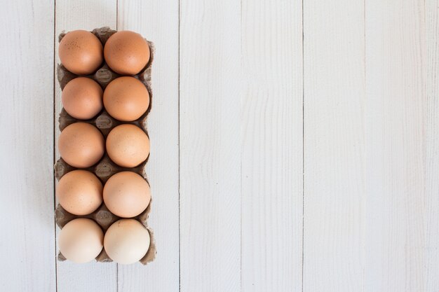 Frische Eier im Kartonpaket auf weißem Holz