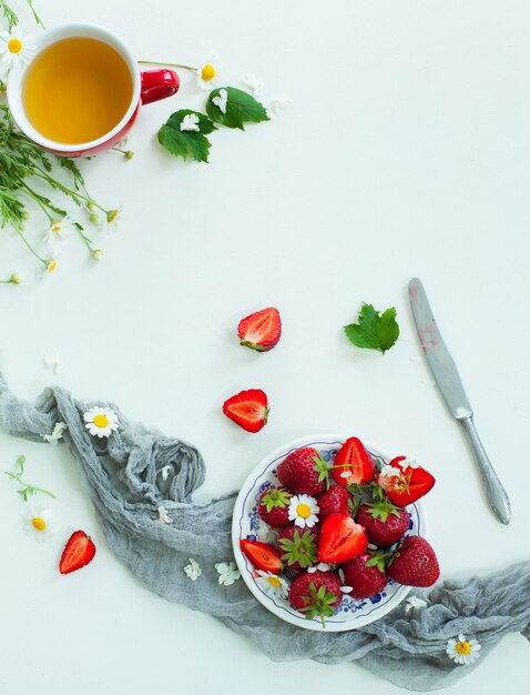 Frische Erdbeerfrüchte, Blumen, Blätter auf weißer hölzerner Tabelle