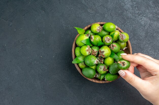 Frische Feijoas der Draufsicht in der weiblichen Hand des Eimers, die Feijoa auf dunkler Oberfläche mit Kopienraum hält