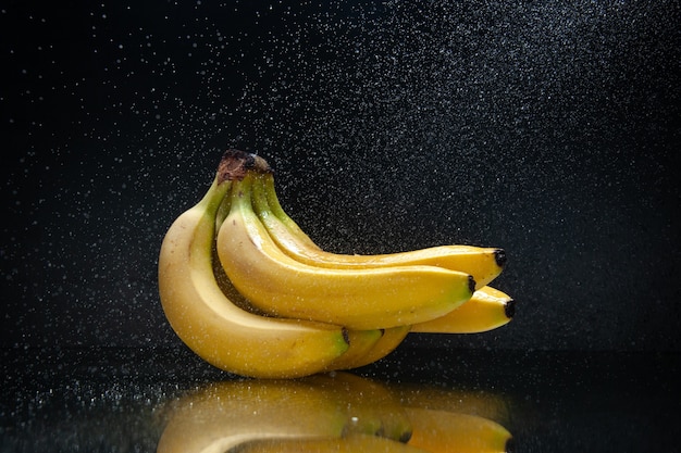 Frische gelbe Bananen der Vorderansicht auf tropischer exotischer Farbdunkelheit der dunklen Hintergrundfrucht