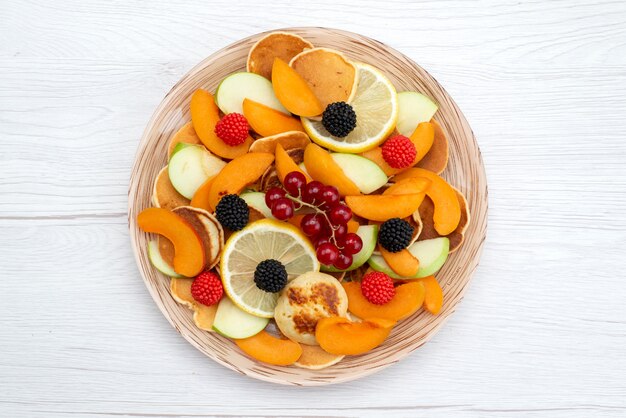 Frische geschnittene Früchte der Draufsicht frisch gefärbt und reif auf dem hölzernen Schreibtisch und dem weißen Hintergrundfruchtfarbfutterfoto