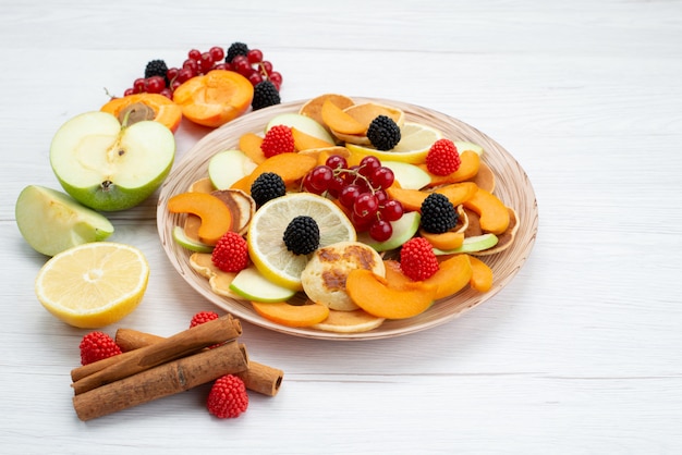 Frische geschnittene Früchte der Vorderansicht bunt und reif auf dem hölzernen Schreibtisch und dem weißen Hintergrundfruchtfarbfutterfoto