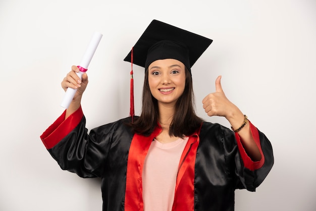 Frische graduierte Frau mit Diplom, das auf weißem Hintergrund aufwirft.
