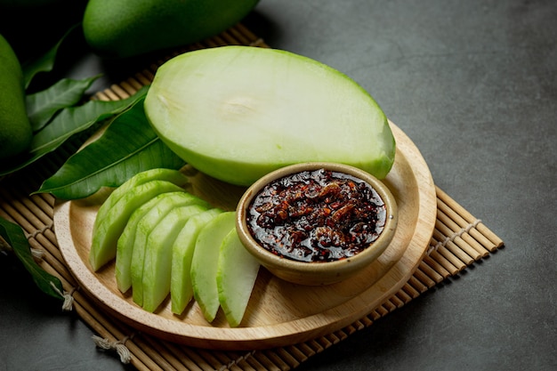 Frische grüne Mango mit süßer Fischsauce, die auf dunkle Oberfläche eintaucht