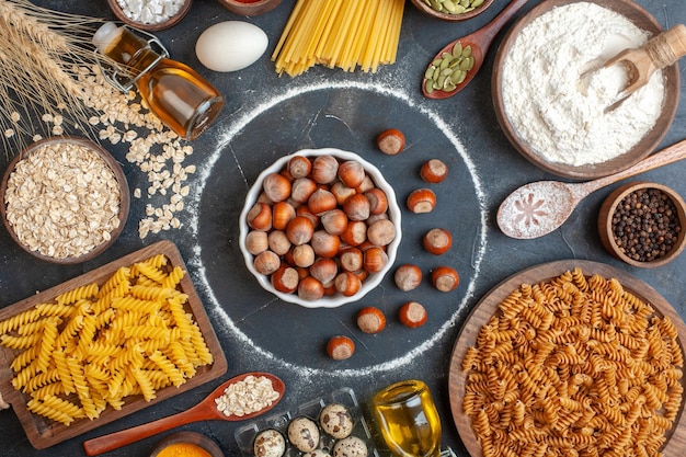 Frische Haselnüsse der Draufsicht mit rohen Teigwarenöleiern und -mehl auf dunklem Hintergrund backen Teigfotomahlzeit-Küchenfarbe