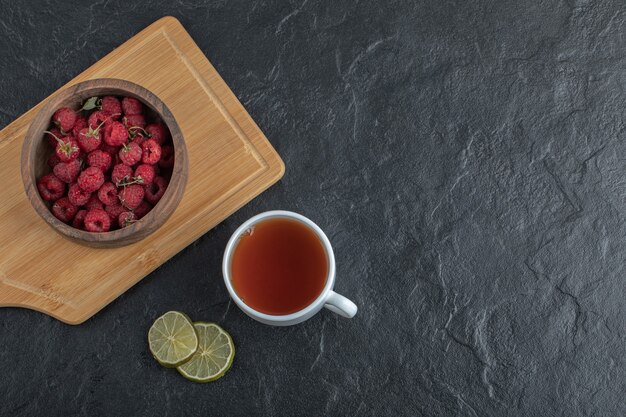 Frische Himbeeren auf Holzbrett mit Tee und Zitrone.