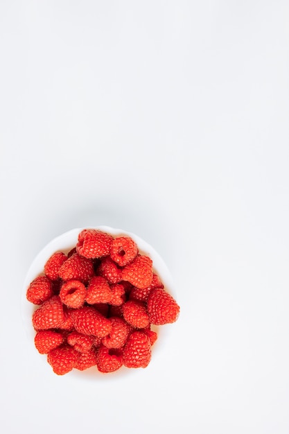 Frische Himbeeren in einer weißen Schüssel auf einem weißen Hintergrund. flach liegen.