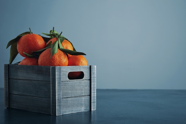 Frische mandarinen in der alten box mit blättern lokalisiert auf rustikalem blauem tisch und seitenansicht des kalten hintergrunds schließen oben