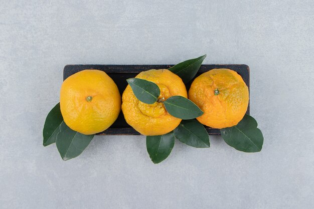 Frische Mandarinen mit Blättern auf schwarzem Teller.