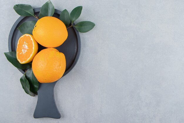 Frische Orangen mit Blättern auf schwarzem Schneidebrett.
