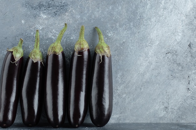 Kostenloses Foto frische organische aubergine in reihe auf grauem hintergrund.