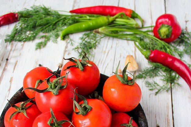 Frische organische rote Tomaten im Schwarzblech auf weißem Holztisch mit den grünen und Rot- und Paprikapfeffern, grünen Paprikas, schwarzen Pfefferkörnern, Salz, Abschluss oben, gesundes Konzept