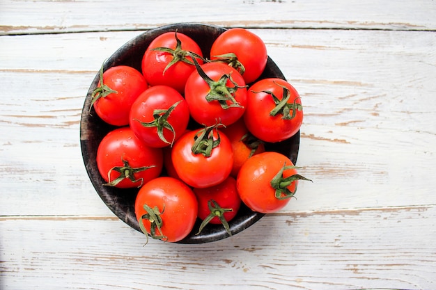 Frische organische rote Tomaten im Schwarzblech auf weißem Holztisch mit den grünen und Rot- und Paprikapfeffern, grünen Paprikas, schwarzen Pfefferkörnern, Salz, Abschluss oben, gesundes Konzept