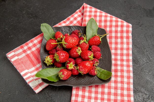 Frische rote Erdbeeren der halben Draufsicht innerhalb der Platte auf dunkler reifer Beere der dunklen Tischfarbe