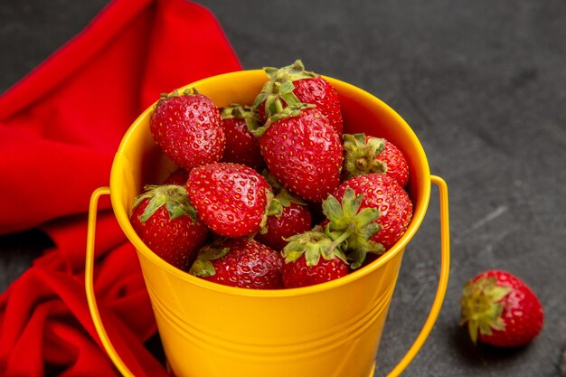 Frische rote Erdbeeren der Vorderansicht innerhalb des kleinen Korbs auf dem dunklen Hintergrund