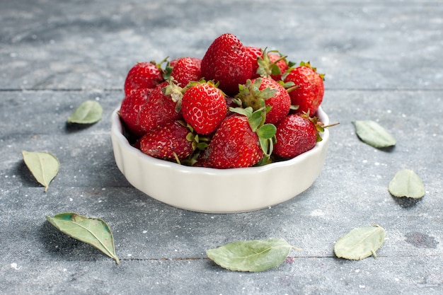 Kostenloses Foto frische rote erdbeeren innerhalb weißer platte zusammen mit grünen getrockneten blättern auf grauem schreibtisch, fruchtfrische beerenfarbfoto vitamingesundheit