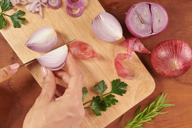 Frische rote ganze und geschnittene Zwiebel. Geschnittene rote Zwiebel mit Petersilie und Rosmarin. Zwiebel und Scheiben auf Holzschneidebrett. frisch gepflückt aus heimischem Bio-Garten. Lebensmittelkonzept.