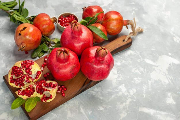 Frische rote Granatäpfel mit halber Draufsicht sauren und milden Früchten auf hellweißem reifem Baum der hellen weißen Schreibtischfrucht