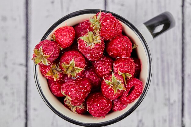 Frische rote Himbeeren auf Becher auf Holztisch.