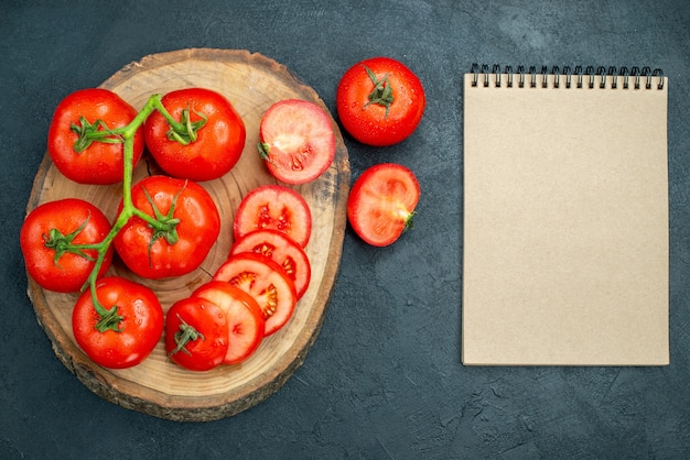 Kostenloses Foto frische rote tomaten der draufsicht auf holzbrettnotizbuch auf dunklem hintergrund