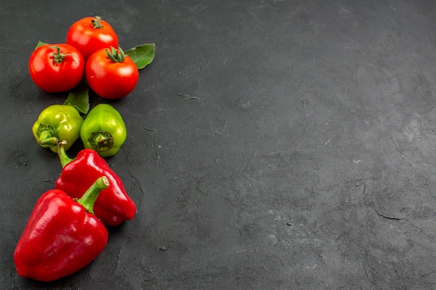 Frische rote Tomaten der Vorderansicht mit Paprika auf dunklem Hintergrund