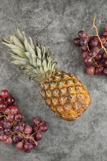 Frische rote Trauben mit reifer Ananas auf Marmoroberfläche.