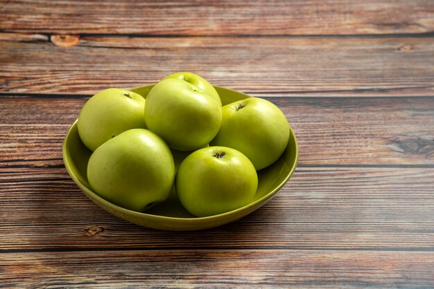 Frische saftige reife grüne Äpfel in der Schüssel auf Holztisch