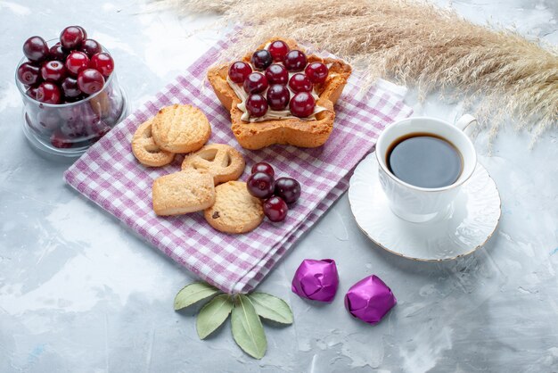 frische Sauerkirschen in Teller mit sternförmigem cremigem Kuchentee und Keksen auf hellem Schreibtisch, Obst-Sauerkuchen-Keks