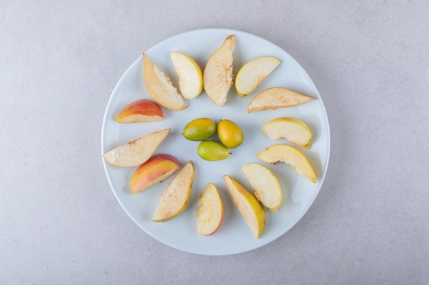 Frische Scheiben Apfel und Kumquats auf einem Teller auf dem Marmor.