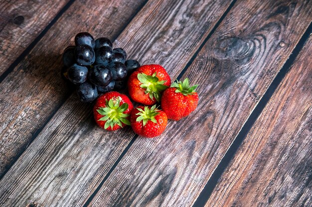 Frische schottische Erdbeeren und schwarze Trauben auf Holztisch.