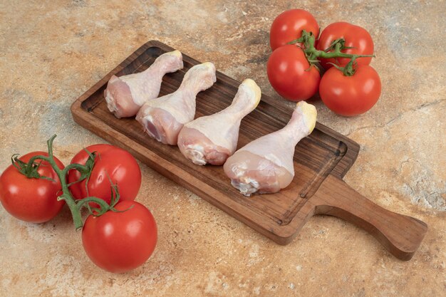 Frische Tomaten mit Holzbrett von ungekochten Hähnchenschenkeln