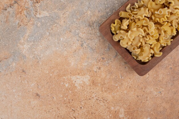 Frische ungekochte Makkaroni auf Holzschale auf Marmorhintergrund