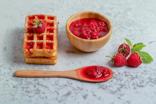 Frische Waffel mit Himbeermarmelade auf grauer Oberfläche.