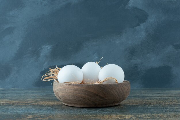 Frische weiße Eier des Huhns, die im Heu auf Holzschale liegen