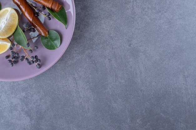 Frische Zitronenscheiben auf lila Platte über grauem Hintergrund.