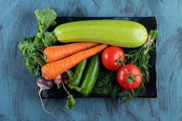 Frische Zucchini, Karotten, Tomaten und Grüns auf schwarzem Teller.