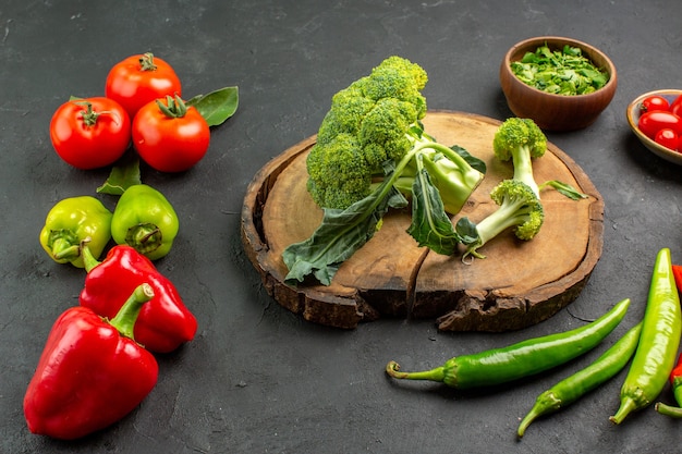 Frischer Brokkoli der Vorderansicht mit Tomaten und Paprika auf dunklem Hintergrund