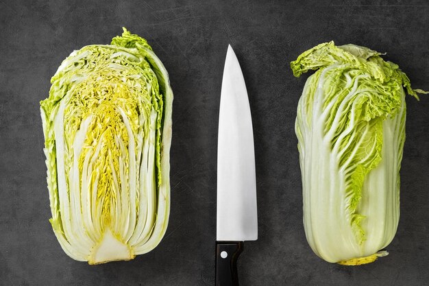 Frischer Chinakohl, ganz und halb, auf einem grauen Tisch neben einem Kochmesser. Anordnung auf dem Tisch, Zubereitung von Salat