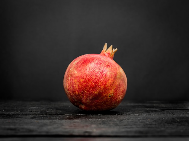 Frischer ganzer Granatapfel auf einem schwarzen Holz schließen