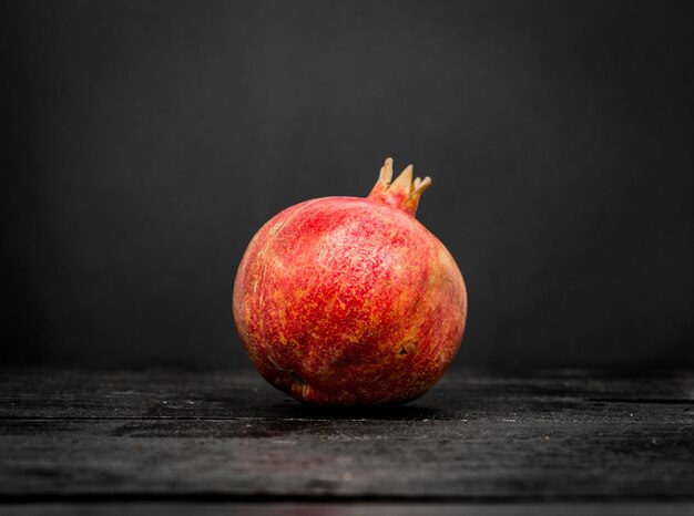 Frischer ganzer Granatapfel auf einem schwarzen Holz schließen