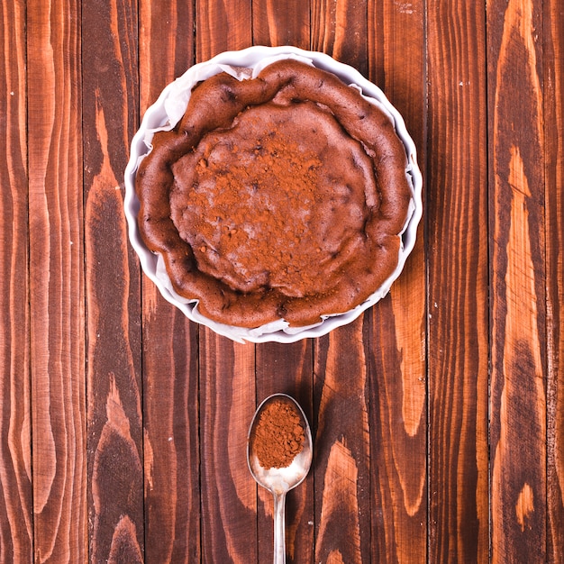 Frischer gebackener Kuchen mit Kaffeepulver im Löffel auf hölzernem strukturiertem Hintergrund