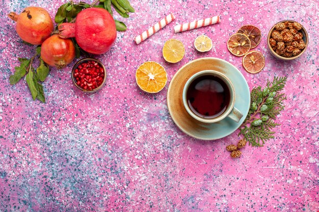 Frischer Granatapfel der Draufsicht mit grünen Blättern und einer Tasse Tee auf dem rosa Schreibtisch